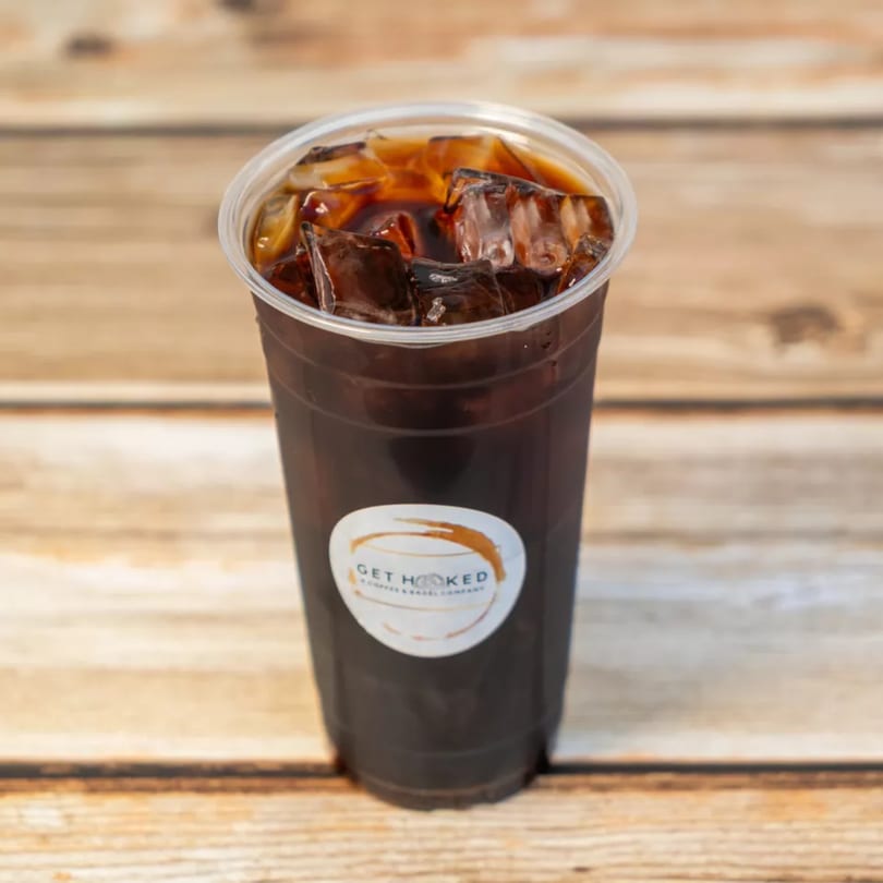 Iced coffee in a clear plastic cup with a "Get Hooked" logo on a wooden surface.