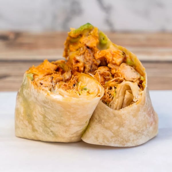 Two halves of a chicken wrap, filled with shredded chicken, sauce, and green vegetables.