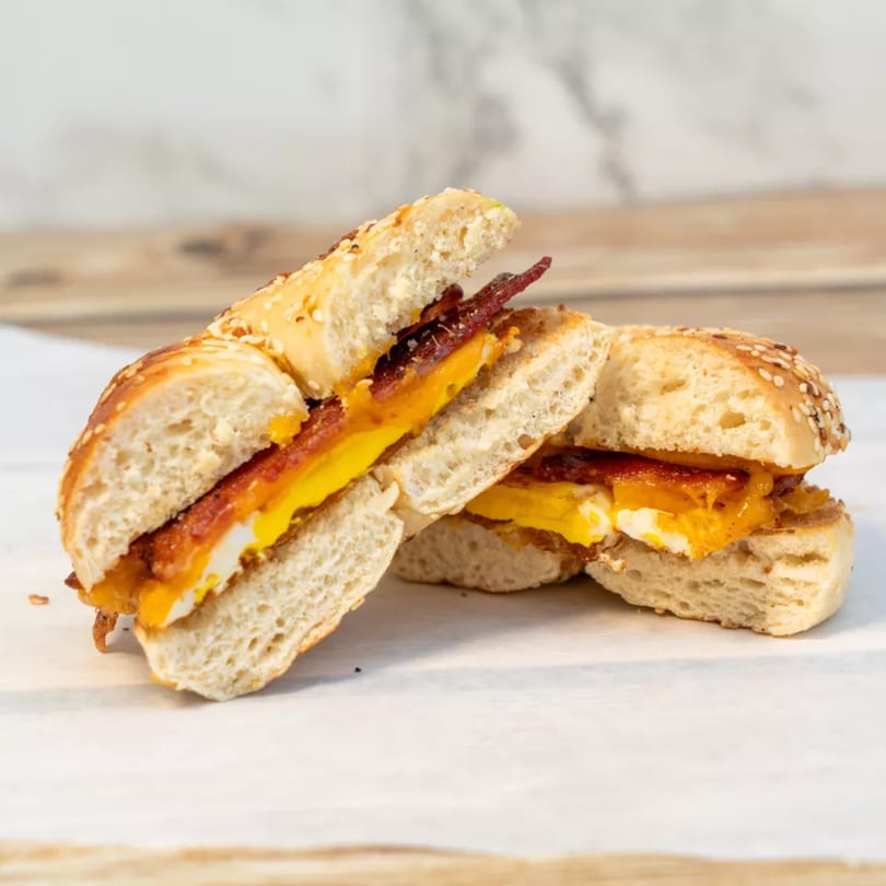 A sesame bagel breakfast sandwich, cut in half, filled with egg, cheese, and bacon.