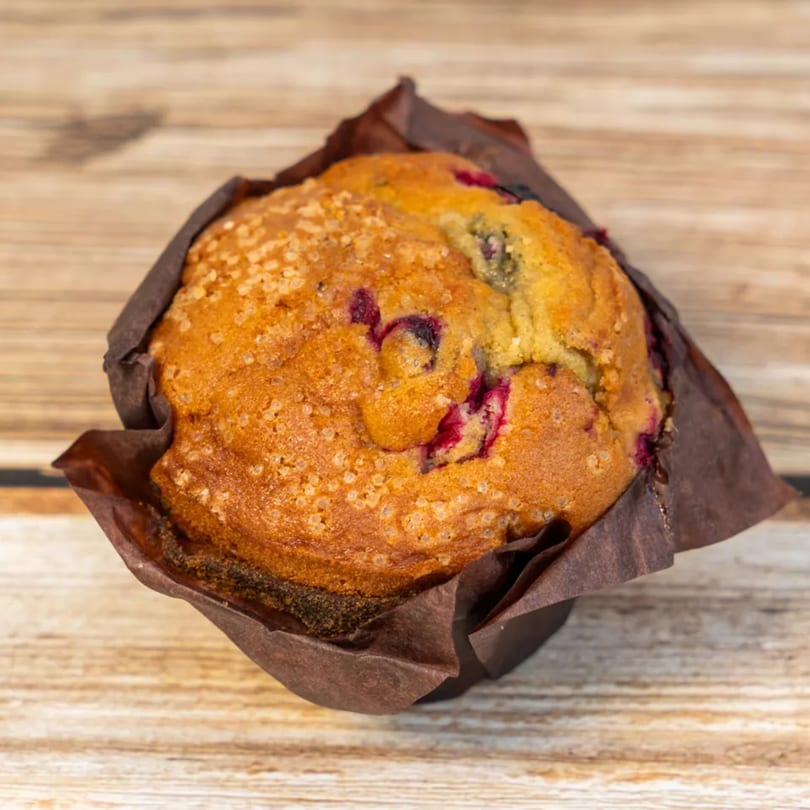 A golden-brown muffin with berries and sugar crystals in a dark brown paper liner on a wooden surface.