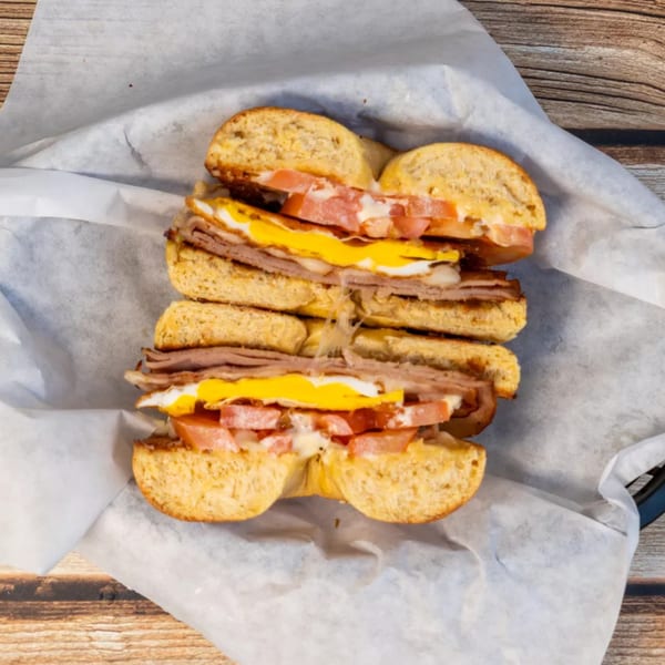 Two halves of a bagel sandwich with roast beef, fried egg, melted cheese, and tomato.