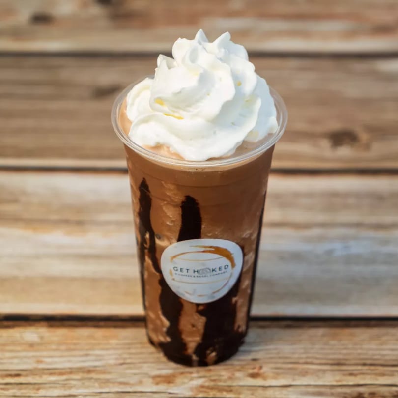 A Get Hooked Coffee & Bagel Company iced mocha with whipped cream on a wooden table.
